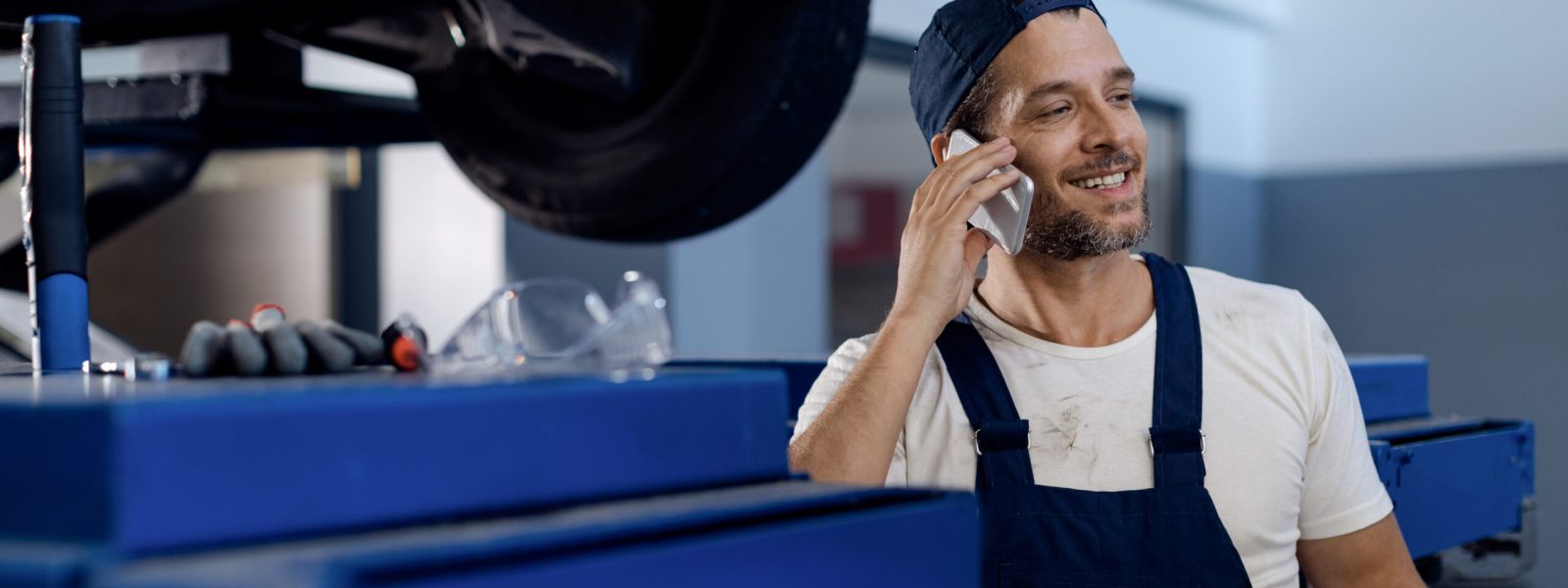 Happy car repairman communicating over mobile phone while working in a workshop.